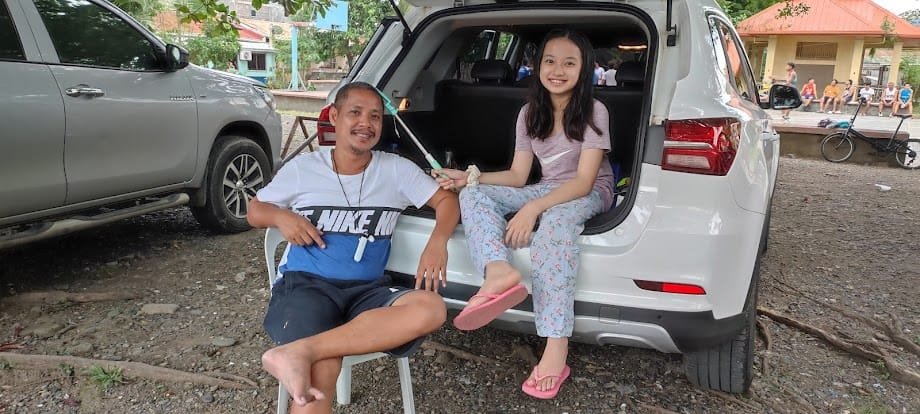 Papa Lenslo and Chloe smiling near a vehicle.
